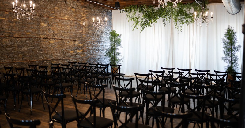 An elegant indoor event space with rows of black chairs facing a white draped backdrop