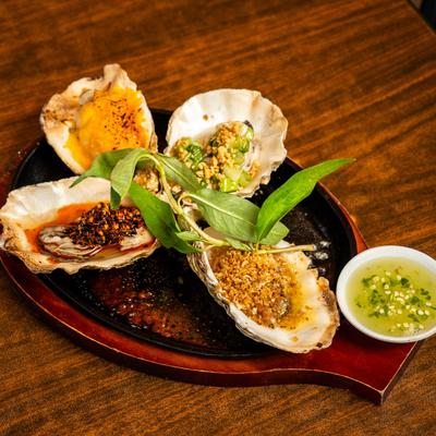 Four flavors of grilled oysters on a skillet with a cup of sauce on the side.