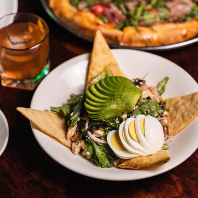 Salad with sliced avocado, boiled egg, and tortilla chips on a white plate.