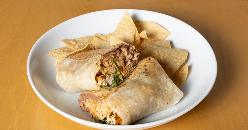 Chicken burrito cut in half, served with a side of tortilla chips on a white plate
