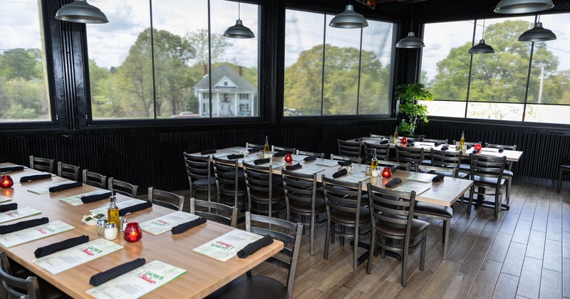 Indoor dining area with tables set for service, large windows showing outside greenery