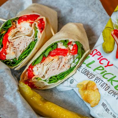 Turkey wrap served with a pickle spear and a bag of spicy pickle dill chips.