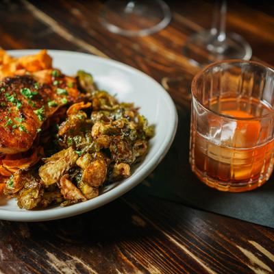 Roasted chicken served with vegetables on a white plate next to an Old Fashioned cocktail.