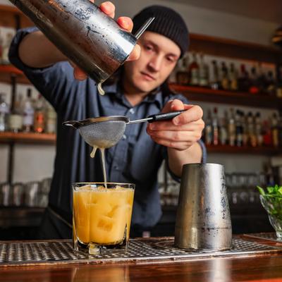 Bartender straining a cocktail into a glass with ice.