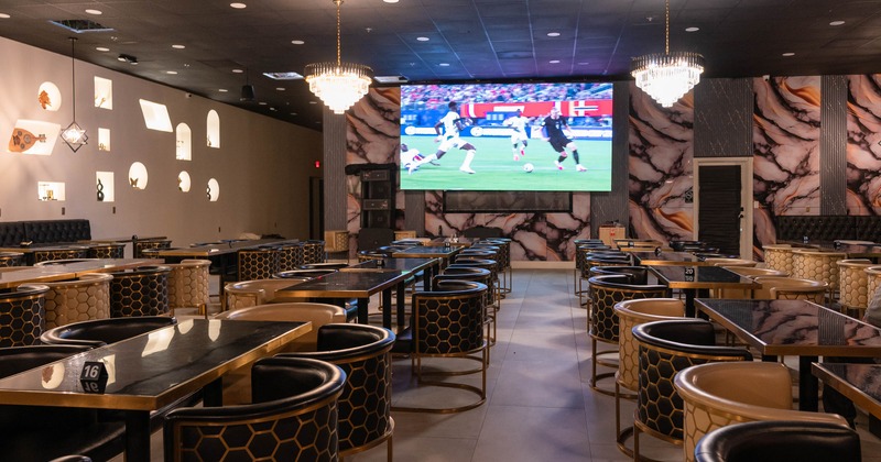 Interior of a modern dining venue with honeycomb-patterned chairs, black tables, and a large TV
