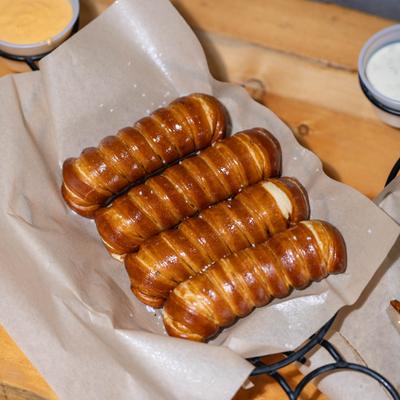 Four soft pretzel sticks served on parchment paper with dipping sauces nearby.