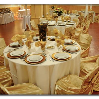Gold chairs surround white tables topped with decorative plates and folded napkins.