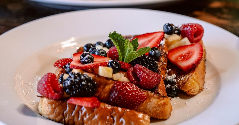 French toast topped with berries, slices of banana and powdered sugar