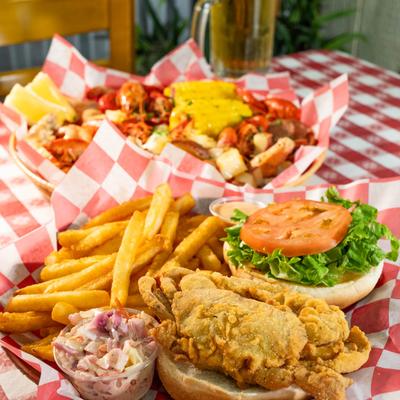 Soft-shell crab sandwich with fries, shrimp slaw, and seafood boil in the background.