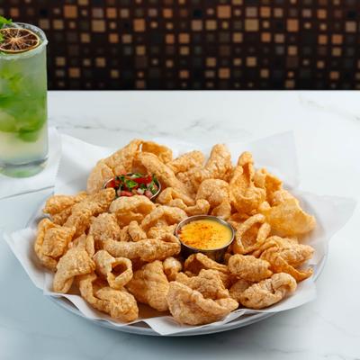 Bowl of crispy fried pork rinds served with cheese dip and a mojito.