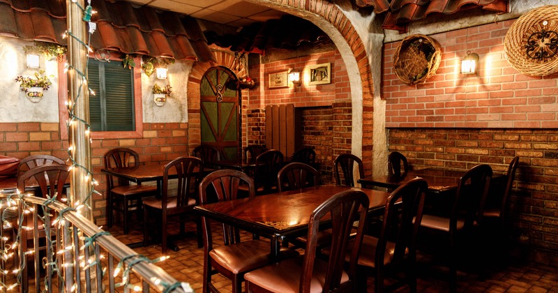 Interior with dark wood tables and chairs, brick walls, terracotta-tiled arches, and soft string lights