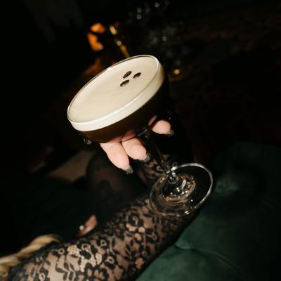 A hand holds a frothy espresso martini with coffee beans on top.