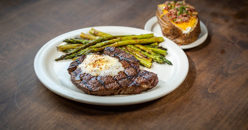 Grilled steak topped with melted butter, served with asparagus and loaded potato