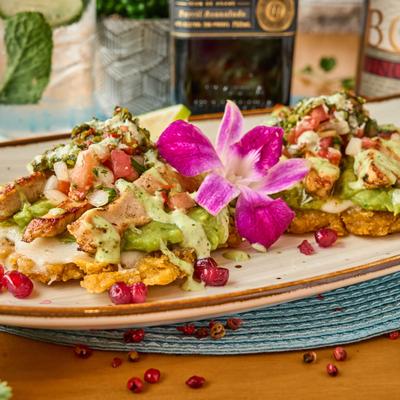 A plate of tostones topped with chicken, guacamole, salsa, and pomegranate seeds.