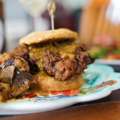 A close-up of a fried chicken sandwich with melted cheese, served with crispy potatoes.