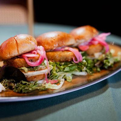 Mini sliders with lettuce and pickled onions on a platter.
