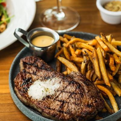Grilled steak topped with butter, served with fries and sauce on the side.