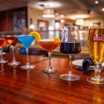 A variety of cocktails and  glasses of beer and wine on a wooden table in a restaurant setting.