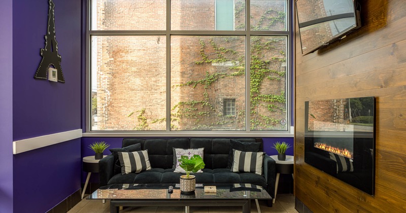 Interior, comfy couch by a window with table in front and electric fireplace and TV