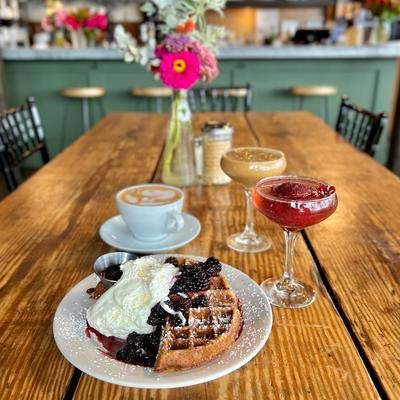 Blackberry whipped cream waffles and latte served with cocktails on a table inside'.