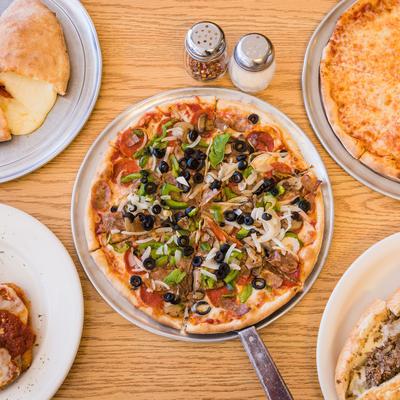 Marina's Supreme pizza sits in the center of a wooden table, surrounded by assorted dishes.