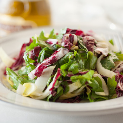 Arugula salad, with radishes, endives, and vinaigrette dressing, closeup.