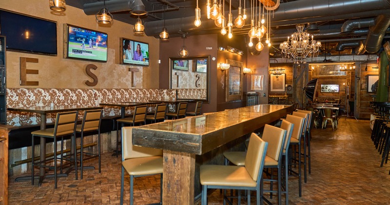 Modern bar interior with a long wooden table, leather chairs, pendant lights and TV screens