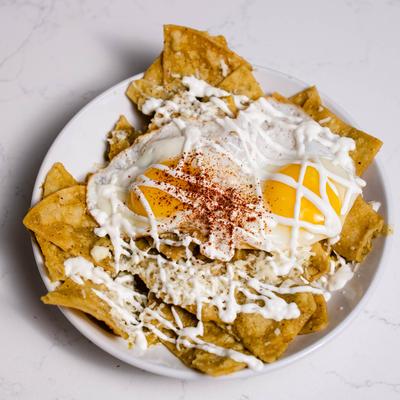 Tortilla chips with green salsa, cheese, cream, and fried eggs.