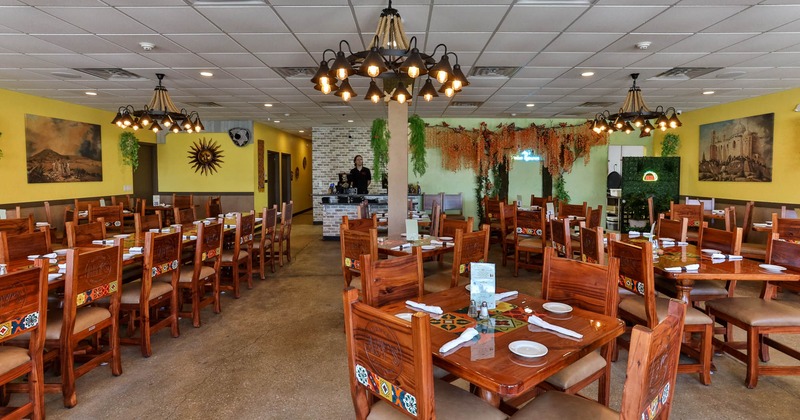 Interior of a restaurant with wooden tables and chairs, chandeliers, yellow walls with artwork