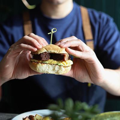 A person holding a sandwich with beef and egg.