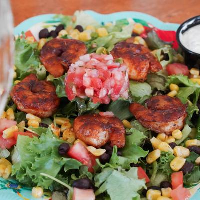 A salad with blackened shrimp, grilled corn, black beans, lettuce, and tomatoes.