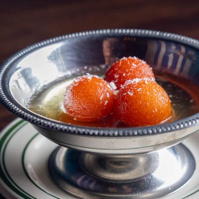 Silver dessert cup filled with Gulab Jamun, placed on a white plate with green stripes.