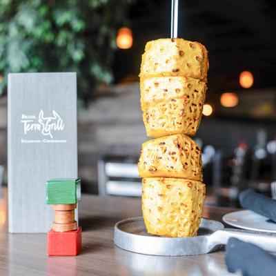 A skewer of glazed pineapple sits on a dining table with the restaurant menu.