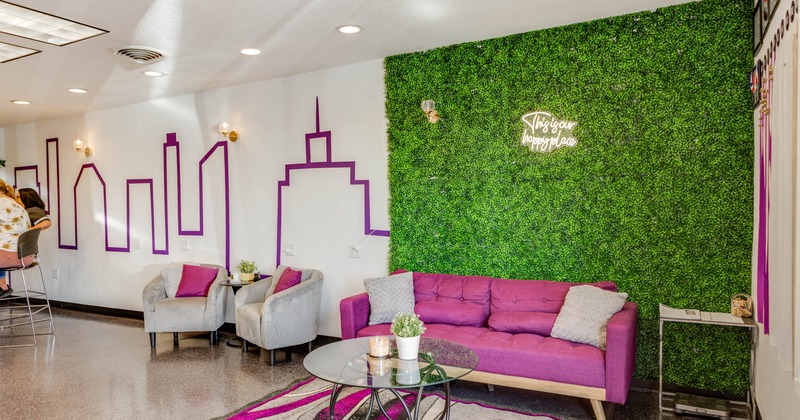 Seating area, pink and grey sofas, armchairs, and cushions, artificial grass wall