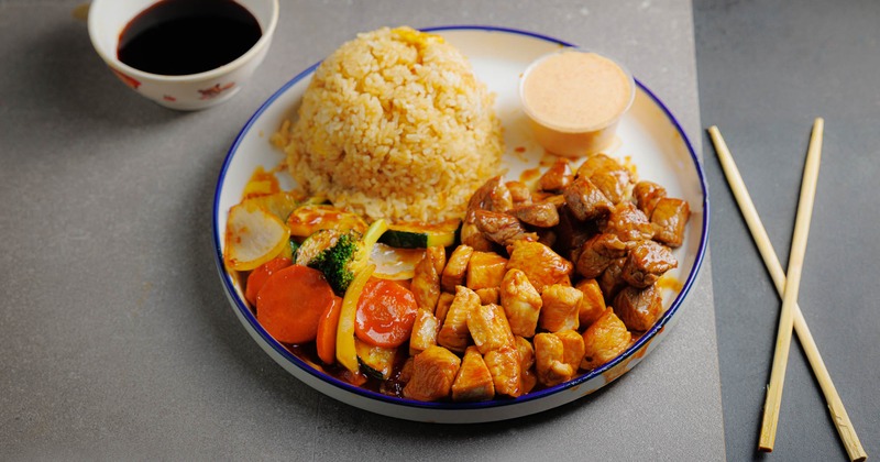 Grilled chicken and steak with rice, vegetables, and soy sauce on the side