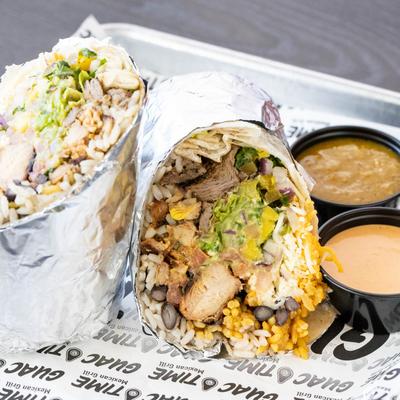 A halved burrito with meat, rice, beans, and sauces on the side.