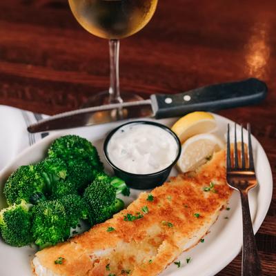 Cracker crumb-coated fish filet with broccoli, dipping sauce, lemon, and white wine.