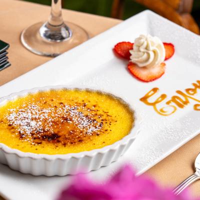 Creme Brulee dessert featuring a side of whipped cream and sliced strawberries.