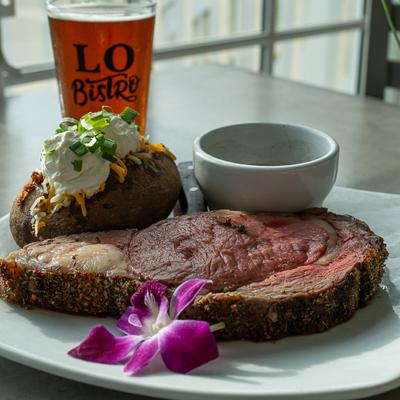 A thick prime rib slice with baked potato and beer.