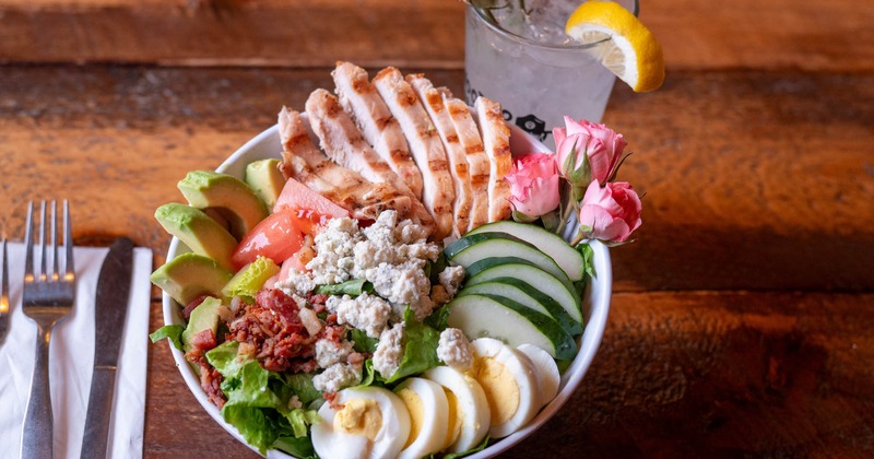 Cobb salad garnished with fresh pink roses, served with a cocktail