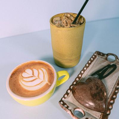 Hot latte with latte art and iced coffee in yellow cups beside a decorative tray.