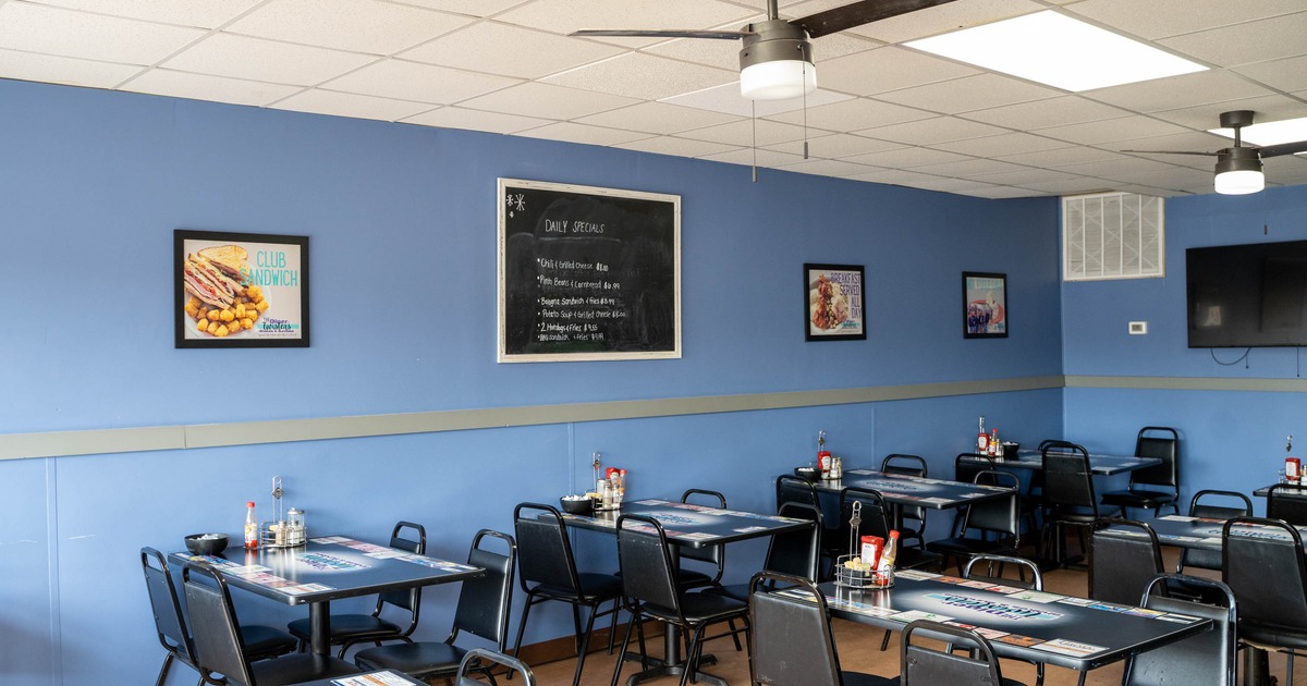 Dining restaurant interior with light blue walls, black tables and chairs, and a chalkboard menu