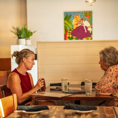 Two patrons chat at a restaurant table with drinks and menus.