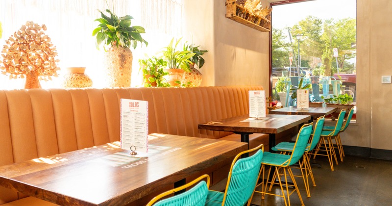 Interior of a restaurant with brown upholstered benches, teal chairs, wooden tables