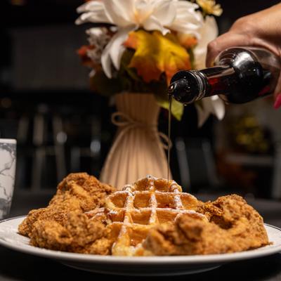 Plate of chicken and waffles with syrup being poured over it.