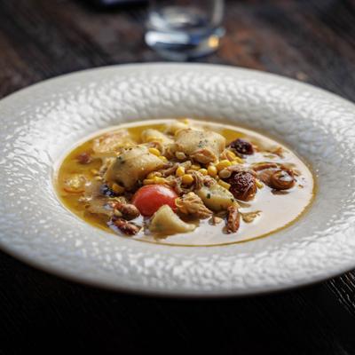 A white textured plate of golden stew with chicken, corn, vegetables and mushrooms..