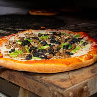 A pizza with various toppings being removed from an oven with a metal paddle.