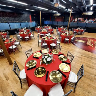 Indoor banquet hall arranged with multiple round tables covered in red tablecloths.