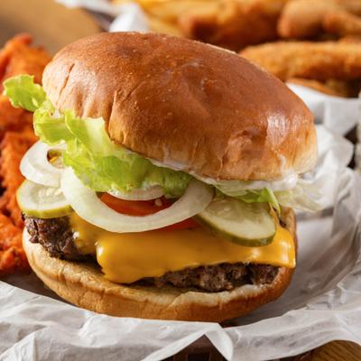 Cheeseburger topped with pickles, lettuce, onion and tomato, close-up.