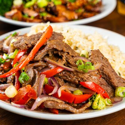 Beef stir-fry with peppers, onions, and rice on a white plate.